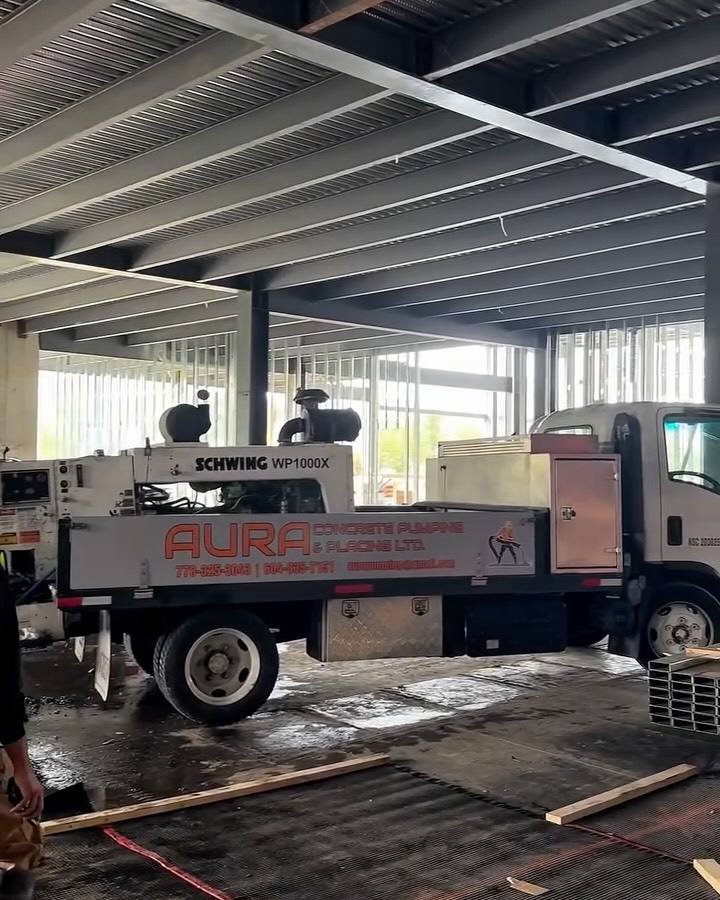 Aura concrete pump truck parked under a new steel-framed building, ready for a slab pour