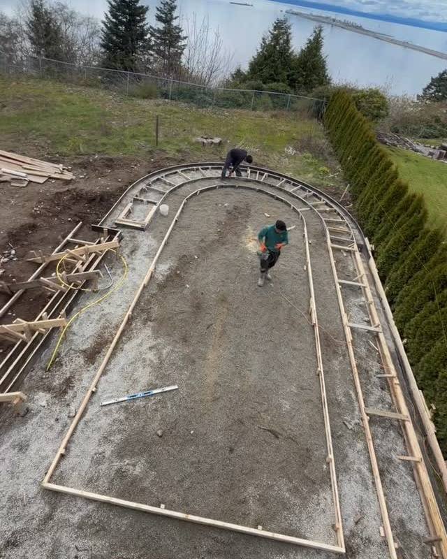 Crew setting curved concrete forms on a hillside lot above the water in Delta